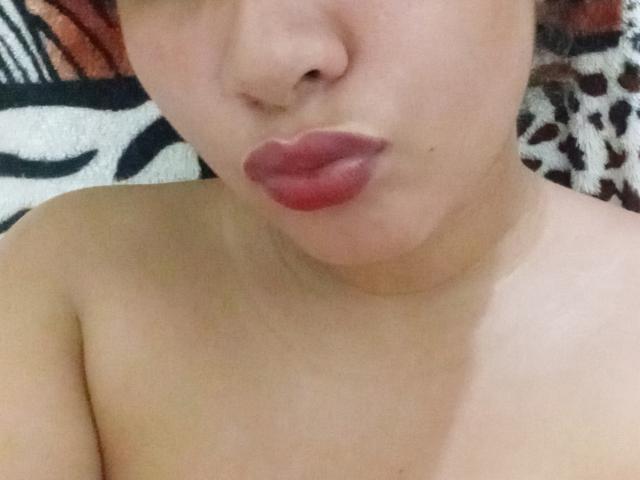 YaraOk's pouty red lips are slightly up, showing off her bare shoulders and smooth, light brown skin. Her nose is small and her face is partially visible.