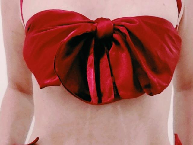 NewCrystal's red satin bow-tie bikini top with large, center knot, covering her tits, showing a fair-skinned, flat stomach, and thin, bare arms, in a tight, close-up shot.