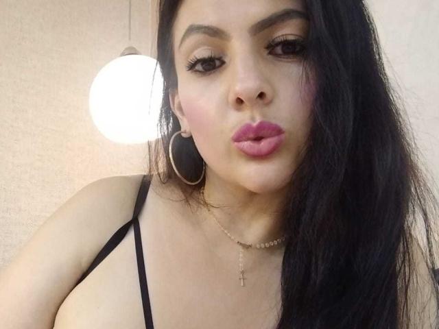 JakyKidman has black hair, pink lipstick, and is pouting with eyes half-open. She's wearing a black strap top, hoop earrings, and a cross necklace.