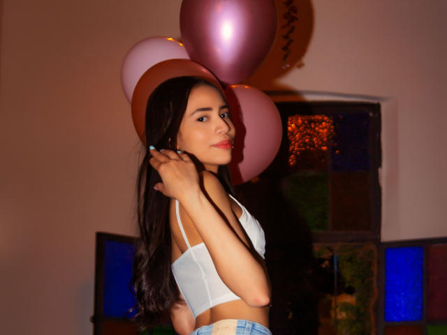 KendallParker with long dark hair, white bra, holding pink and purple balloons, looking over shoulder, soft lighting, confident expression, slightly curved ass, indoors.