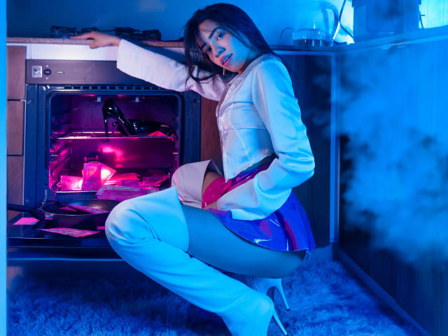 KendallParker, Asian woman with long black hair, white thigh-high boots, and white sweater, squatting in front of an oven with pink and blue neon lights, showing her ass.