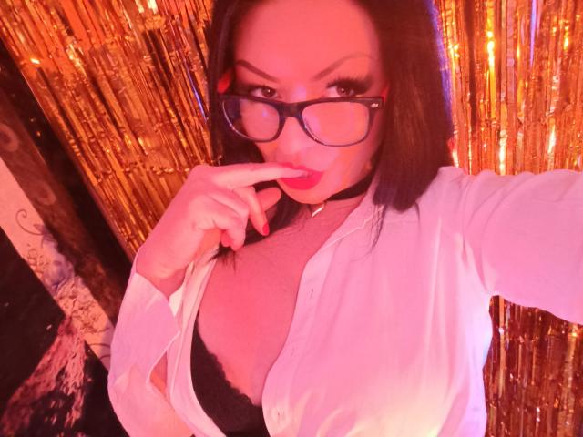 AmberSunshine with glasses, pink lips, and red nail polish, finger in mouth, white shirt open, black bra, showing tits, dark hair, choker, gold curtain, pink light.