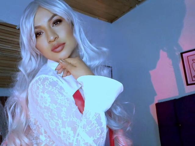 CarlaMuille with white lace top, red tie, long wavy white hair, pink lips, looking at camera, hand near face, soft blue lighting, shadow on wall, sexy, cute.