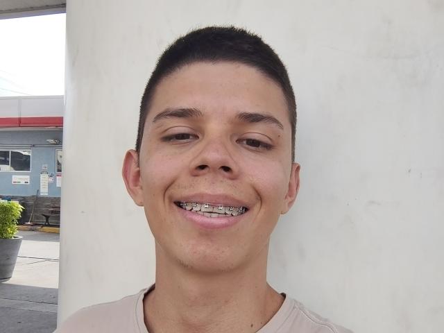 JhoanVelezX has a short, dark haircut, brown eyes, and a silver brace on his teeth. He's smiling with light skin and a beige shirt.