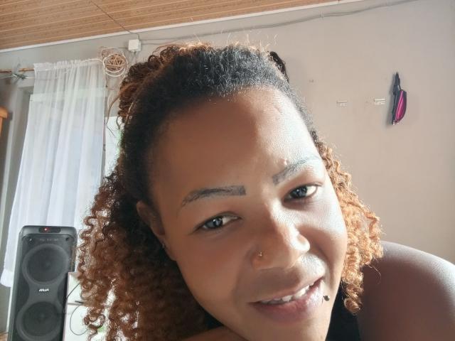 Araf, a curly-haired woman with light brown skin, a nose ring, and a lip piercing, smiling at the camera, showing her small, slightly upturned nose and full lips.