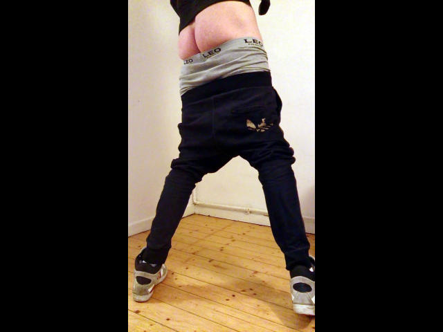 Defender-hot's ass is exposed, black jeans pulled down to show gray underwear, black socks, and gray sneakers on a wooden floor.