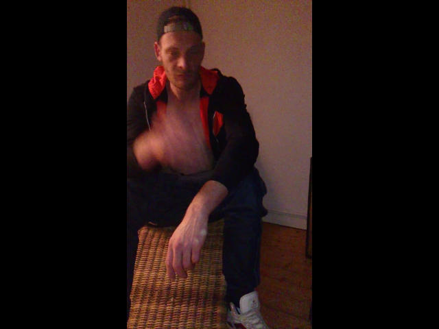 Defender-hot with short dark hair, wearing a black jacket with red lining, blue pants, and white sneakers, is shirtless and leaning forward with a blurred, raised hand.