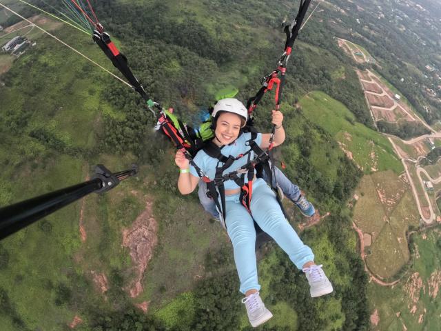 ZoeTobon69 is in a harness, wearing a white helmet, blue shirt, and light blue pants, with white sneakers, flying through the air on a zipline, smiling.