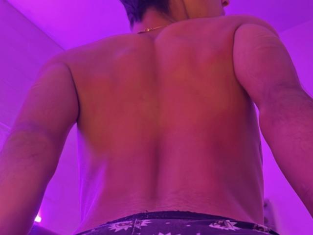 MatthSexy's back is shown, shirtless, with visible muscles and a tan line. He's wearing dark underwear with a white pattern. Purple lighting. 

 