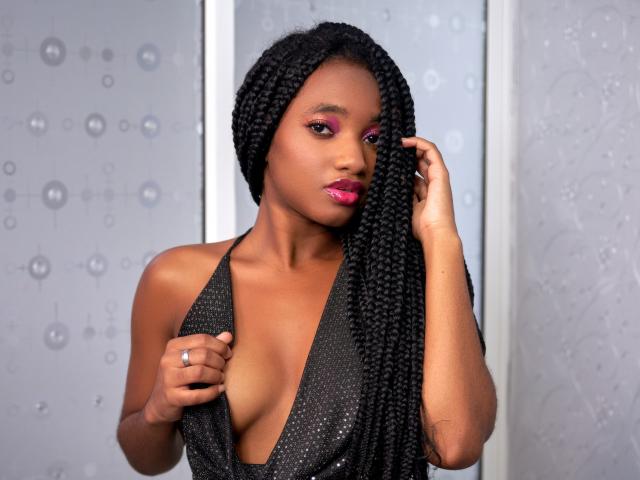 EmmaParisi with dark skin, long braided hair, wearing a sparkly black halter top, exposing her small tits, pink eyeshadow, and pink lipstick, touching her hair.