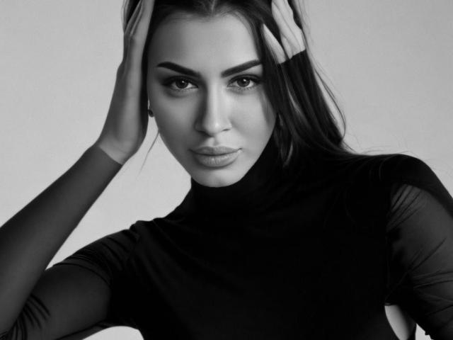 LuisaAh with hands in long dark hair, wearing sheer black top, serious expression, greyscale, her tits slightly visible, high-contrast, her ass not visible, no text.