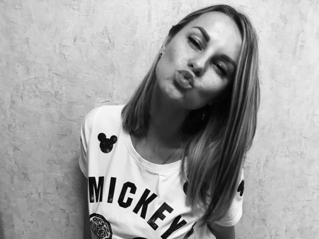 BelleLisaG, avec ses lèvres pulpeuses, sa tête légèrement inclinée et ses cheveux mi-longs, portant un t-shirt "MICKEY", a un look mignon et sexy, ses petites seins étant visibles sous le t-shirt. Noir et blanc..