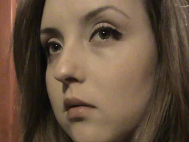 BigLovelyBoobs has a pensive expression with subtle makeup, long eyelashes, and light brown hair. Her slightly parted lips and serious eyes dominate the image.