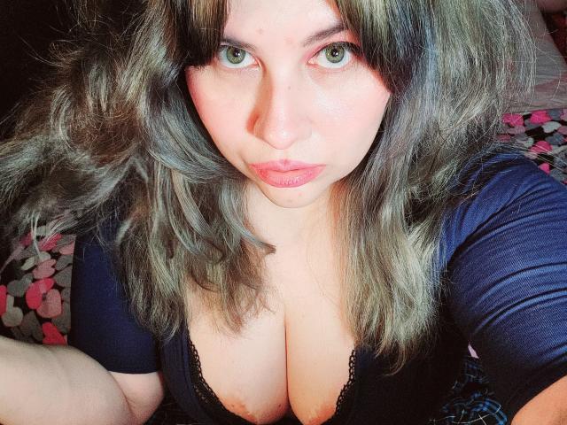 Akkanee tiene ojos verdes, cabello ondulado de color grisáceo-marrón y una expresión seria, y lleva puesto un top negro con encaje que deja ver sus grandes senos pálidos..