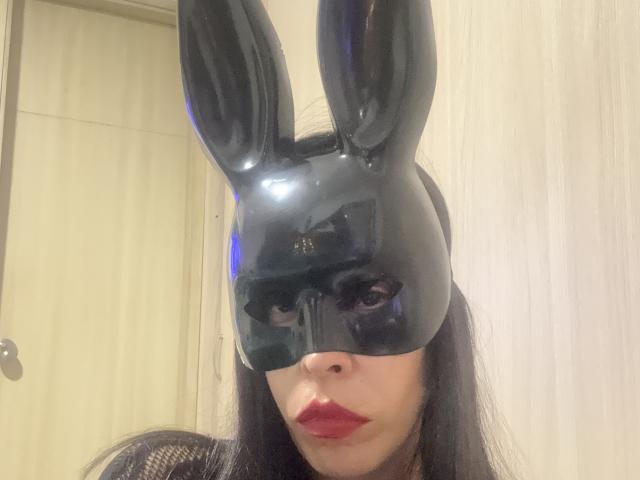 SeleneBrigth wears a shiny black bunny mask with tall ears, red lipstick, and long black hair, showing her pouty face in a selfie. Her ass is not visible.