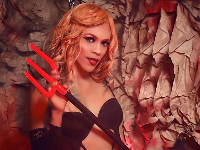 Kendall Taylor, con cabello rubio ondulado, sostén un sujetador negro, sosteniendo un tridente rojo, luciendo sexy, usando guantes negros sin dedos, lápiz labial rojo y maquillaje sutil, en una pose provocativa y diabólica..