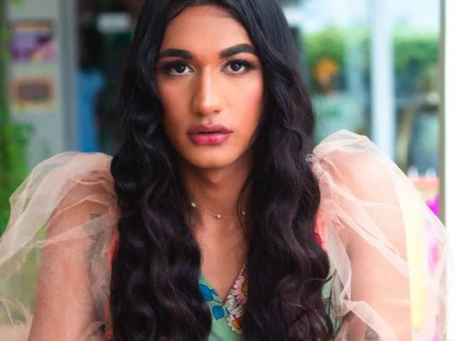 Alexa69s with long, wavy black hair, wearing a sheer, puffy-sleeve dress, has full lips and dark, thick eyebrows. She's staring directly at the camera with a serious look.