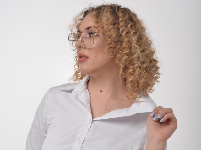 ArishkaLulu with curly blonde hair, glasses, white shirt, and blue nails, holding shirt collar, side profile, looking to the left, slightly parted lips, fair skin, small mole.
