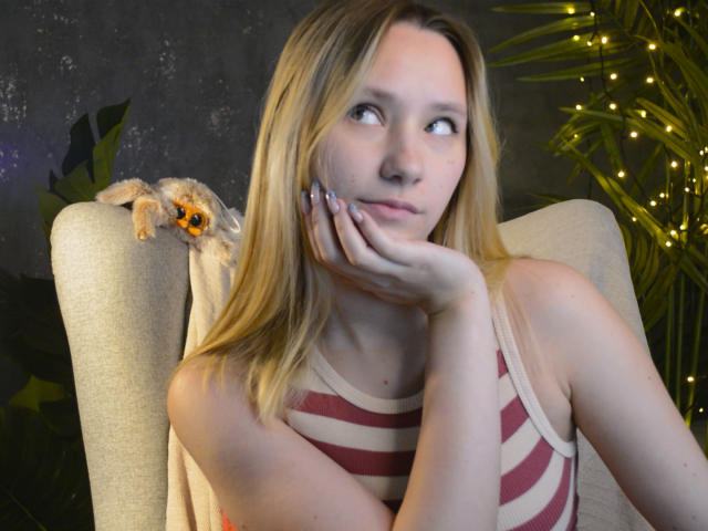 CaramellSex with blonde hair, red-striped tank top, hand on cheek, looking to the side, small fuzzy orange and brown critter on chair's back, green plant and yellow fairy lights.