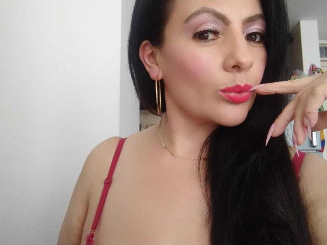 JakyKidman, mit pinkem Lippenstift und langen schwarzen Haaren, berührt ihre glänzenden roten Lippen mit einem Finger, trägt rote Dessous und goldene Ohrringe und zeigt ihr süßes, sexy Gesicht..