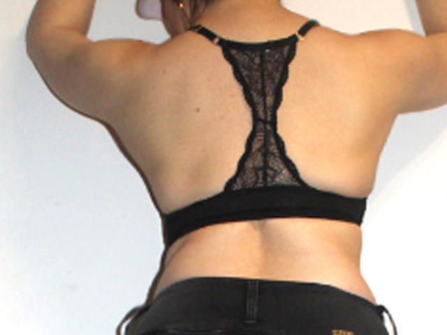 PriscillaHotMature's back, wearing a black lace bra, exposing her bare back and upper ass, with black pants, arms raised. She has a fit, toned, tan body.