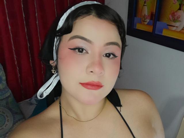CassandraSexy with pale skin, black hair in a white headband, pink eyeshadow, black eyeliner, red lipstick, black halter top, necklace, looking at camera, slightly blushed cheeks, sexy face.