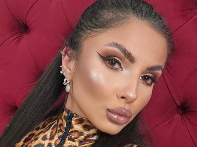 GoddessKaterina has tan skin, brown eyes, and thick, dark eyebrows. She's wearing a leopard print top, eyeliner wings, glossy brown lipstick, and diamond earrings.