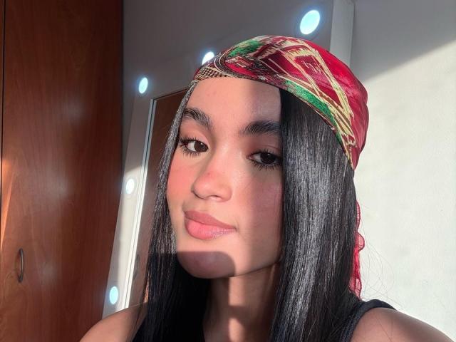 Miia Palmer ha lunghi capelli neri, un foulard rosso e verde e un sorriso carino con labbra rosa. La luce del sole mette in risalto la sua pelle liscia e abbronzata e le sue sopracciglia scure e sensuali..