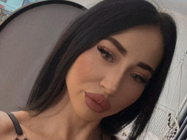 LexyAva has dark, straight hair, thick eyebrows, long eyelashes, and pouty, pinkish-brown lips. She's wearing a black strap, and her nose is slightly upturned.