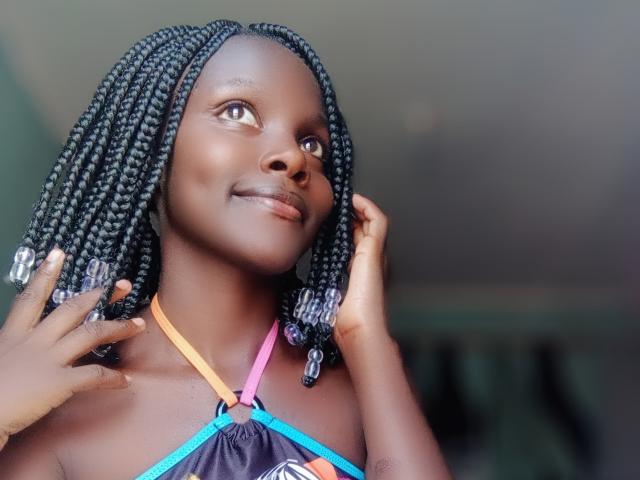SweetSexyBabe with dark skin, braided black hair, smiling, wearing a colorful halter top, hands touching her face, looking upwards. Her tits are small, her ass is not visible.