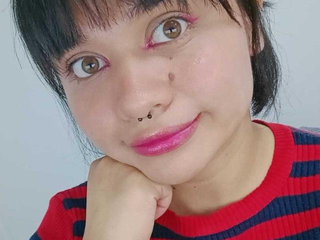 LizyOwen has a cute face with pink lipstick, black nose ring, and small moles. She's wearing a red and blue striped shirt, resting her chin on her hand.