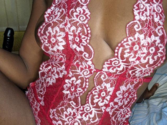 MilaLove69's red lace lingerie with white floral patterns, showing her large, round tits through a deep V-cut. Her dark skin contrasts with the red and white lace.