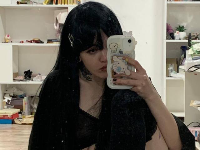 Azusa Nakano mit schwarzen Haaren, die ein Handy mit einer niedlichen Cartoon-Hülle hält, trägt schwarze Dessous, zeigt ihre Brüste, in einem Spiegel-Selfie, in einem unordentlichen Zimmer..