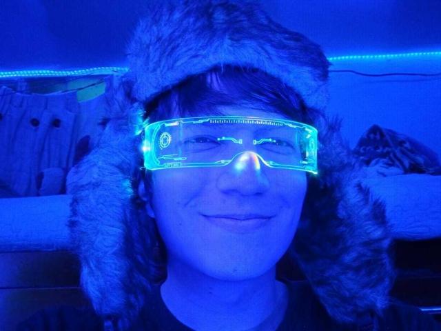 ErossGuy has blue neon visor, fluffy fur hat, and a smug face. His visor glows green, illuminating his white skin and brown hair. He's looking cute, dude.