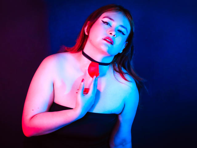 AliaMillers with red lips, blue and pink lighting, black strapless dress, black choker, holding red rose to chest, red nails, slightly leaning back, looking seductively at camera.
