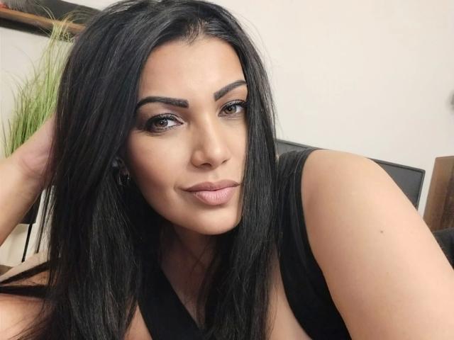 BeliseChappelleX-hot with long black hair, brown eyes, and glossy pink lips, wearing a black sleeveless top, looking slightly to the side with a subtle smile.
