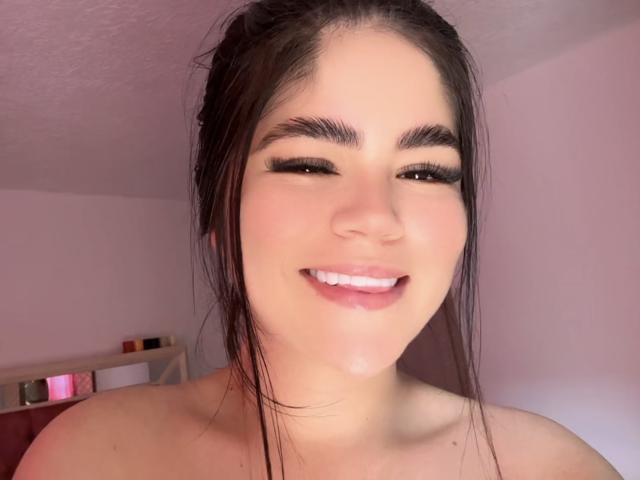 MartinaRossyI has a cute smile with full pink lips, dark eyebrows, long eyelashes, and wet brown hair, showing a small drop of cum on her chin.