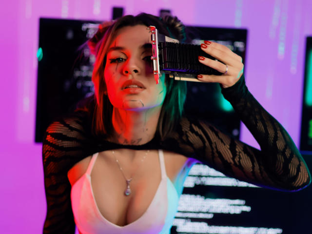 LenaBranch con rossetto rosso e maniche di pizzo nero, che tiene una macchina fotografica all'occhio, con scollatura bianca, collana e pelle umida, illuminata da luci al neon colorate..