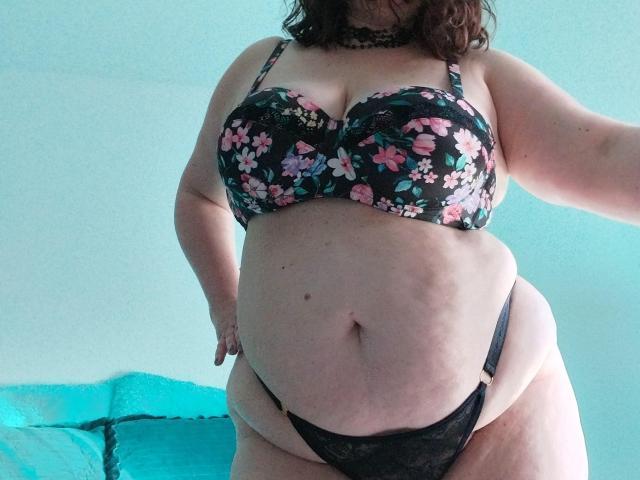 LiliChattePoilue has large, floral-patterned tits in a black bra, and is wearing black lace panties. She's plus-sized with a soft belly and light skin.