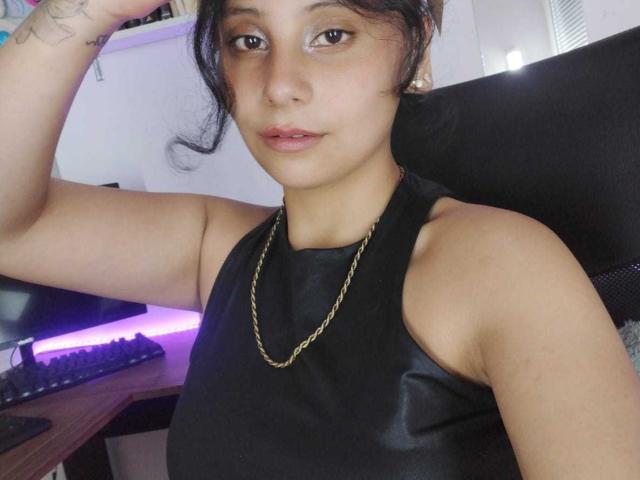 JulietaAkane with light brown skin, black hair, and a nose ring, wearing a black leather halter top and gold chain, looking at the camera with a relaxed expression.