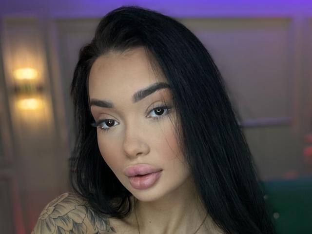SashaFerrera has long black hair, full pink lips, tattooed shoulder, and a sexy face with dark eyebrows and eyeliner. She looks directly at the camera with a slight pout.