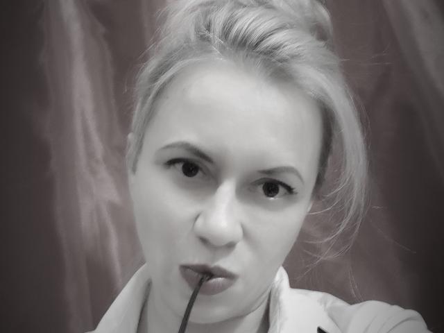RebeccaDarling69 has light blonde hair in a messy bun, holding a black straw in her mouth, with a serious expression, wearing a light shirt, in a grayscale photo.