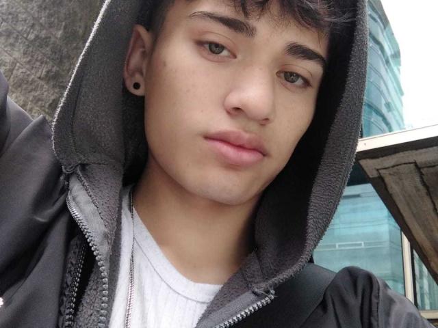 HarryClaude has a cute, chubby face with light brown skin, dark eyebrows, and a small nose. He's wearing a black hoodie, white shirt, and ear gauges. Pouty lips.