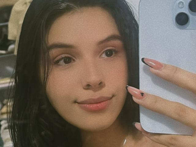 Guadalupe, met zwart haar, lichtbruine huid en roze lippenstift, lacht naar de camera en houdt een telefoon vast. Ze heeft roze nagels, bruine ogen en een schattelijk, aantrekkelijk gezicht..