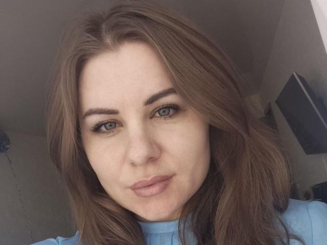 FrostxAngel has light brown, wavy hair, blue eyes, and slightly pouty pink lips. She's wearing a light blue shirt, with subtle makeup highlighting her eyebrows and eyelashes.