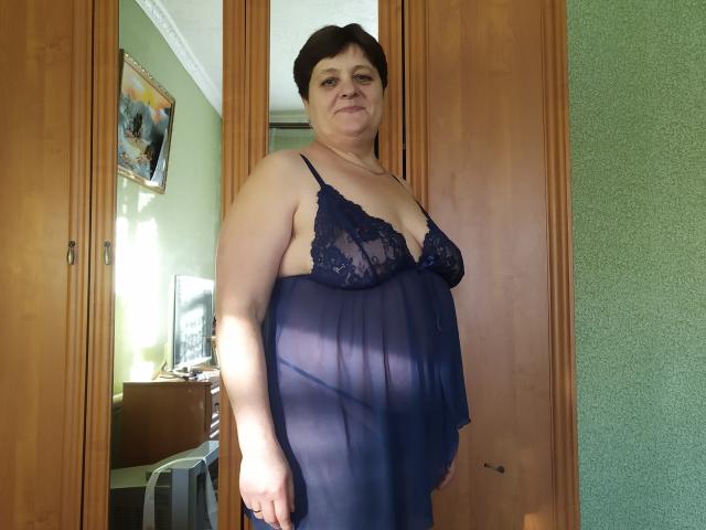 ElzaJewel stands in a doorway wearing a sheer blue lace babydoll, showing her tits and a bit of her ass. She's short-haired, with a neutral expression.