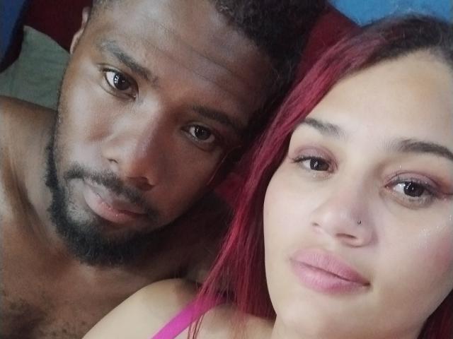 DannyAndLuize, both topless, in a selfie. Danny, a dark-skinned dude with a beard, next to Luize, a light-skinned woman with pink hair and a nose piercing.