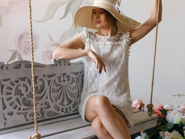 SheillaAdrian sitting on a decorative gray swing wearing a white lace dress and a wide-brimmed hat with pearl details, showing her bare ass and crossed legs.