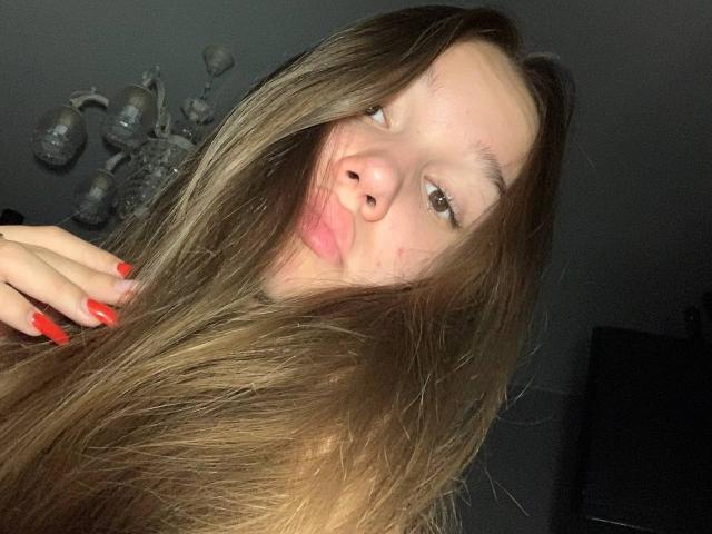 MisaQueen, con i suoi lunghi capelli castani, le unghie rosse e le labbra piene, fa una smorfia, mostrando il suo naso e la sua pelle leggermente lentigginosa in un selfie scattato in un ambiente poco illuminato..