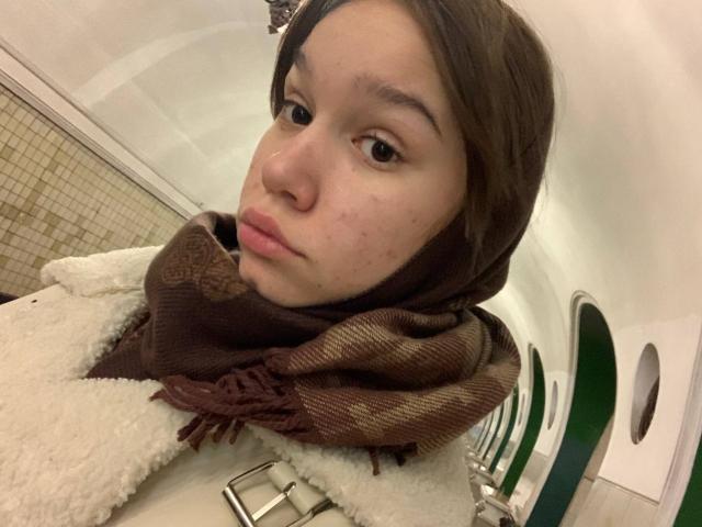 MisaQueen heeft bleke huid, bruine ogen en een bruine sjaal over haar pluizige witte vacht. Haar gezicht vertoont wat acne, en ze kijkt iets opzij met een neutrale uitdrukking..